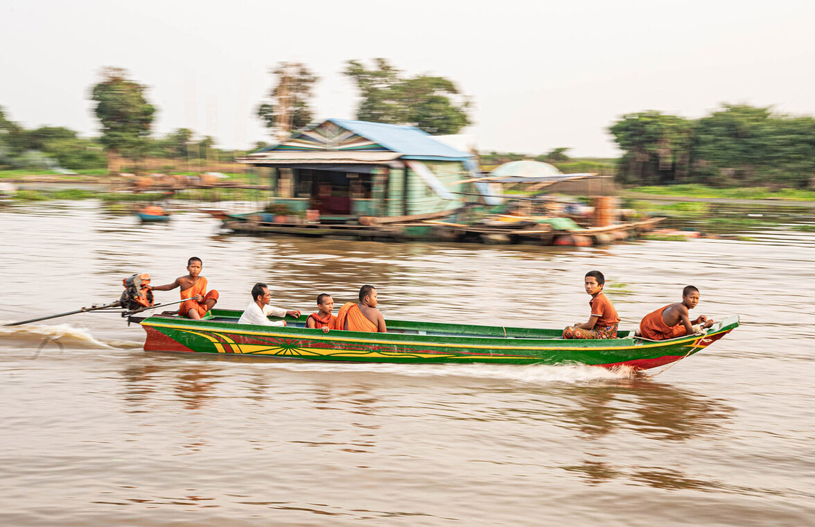 Buddhistische Mönche düsen auf einem Motorboot an einer Hütte auf dem Tonle Sap vorbei