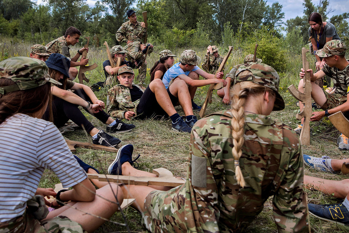 Kinder mit Holzgewehren in Militärkleidung sitzen im Kreis