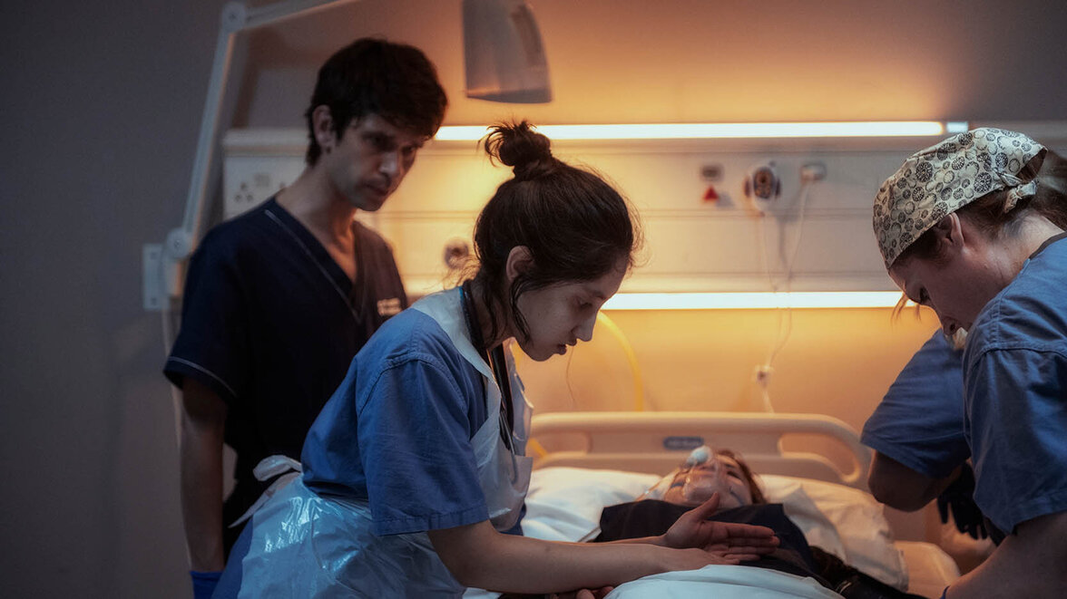 Adam (Ben Whishaw) beobachtet im Hintergrund, wie Shruti (Ambika Mod) eine Patientin in einem Krankenbett versorgt