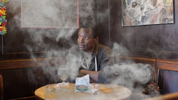 Agomo Atambire, Praktikant bei fluter, sitzt in einer Raucherkneipe