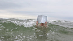 Jemand schwimmt im Meer und liest dabei in einem Laptop wie in einem Buch