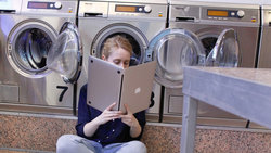 Eine junge Frau in einem Waschsalon halt einen Laptop wie ein aufgeklapptes Buch