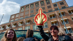 Menschen protestieren vor dem Shell-Firmensitz mit einem Shell-Logo, das den Stinkefinger zeigt