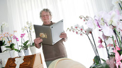 Von Orchideen umringte Frau hält Laptop wie ein Buch und liest darin