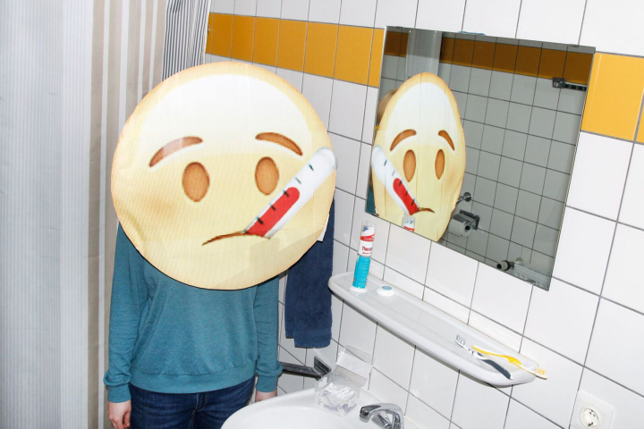 Emoji mit Fieberthermometer im Mund steht vor dem Badezimmerspiegel