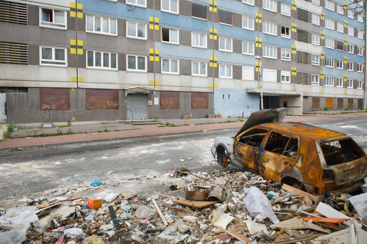 Schutthalde und Autowrack vor Wohnblock in der Pariser Banlieue