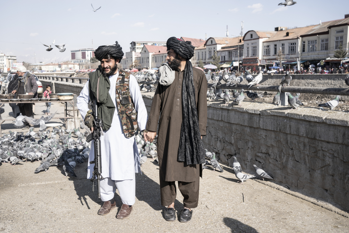 Zwei bewaffnete Taliban lassen sich Händchen haltend auf einer Brücke voller Tauben fotografieren