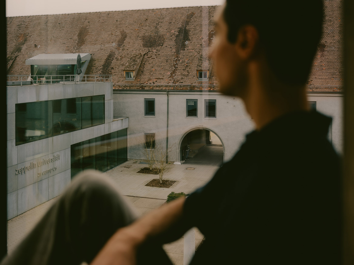 Ferhat sitzt auf der Fensterbank und blickt auf den Campus der Uni