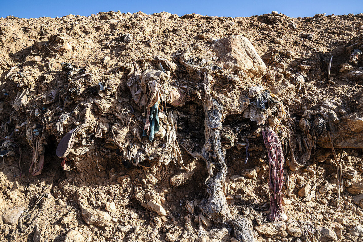 Knochen und Kleidungsstücke in den Erdschichten eines Massengrabs