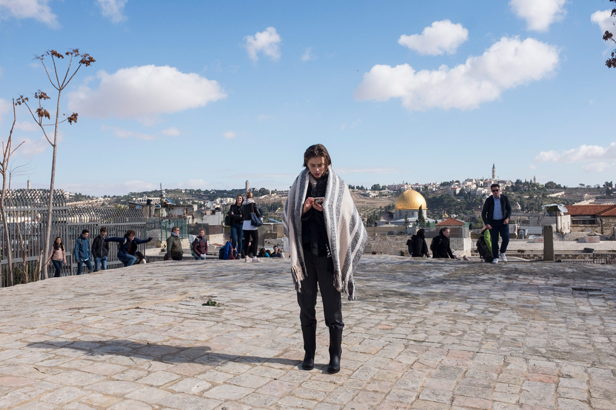 A model checks her smartphone during a break from a fashion shooting on the roof tops. In the background the golden dome of the Dome of the Rock