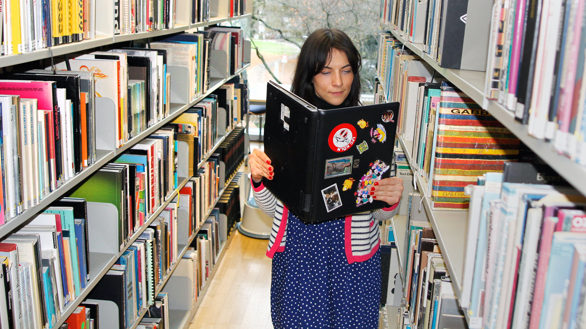 Fraus in einer Bibliothek liest in ihrem Laptop Fraus in einer Bibliothek liest in ihrem Laptop