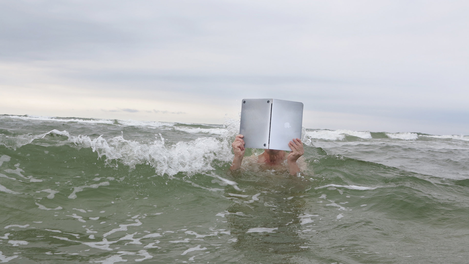 Jemand schwimmt im Meer und liest dabei in einem Laptop wie in einem Buch