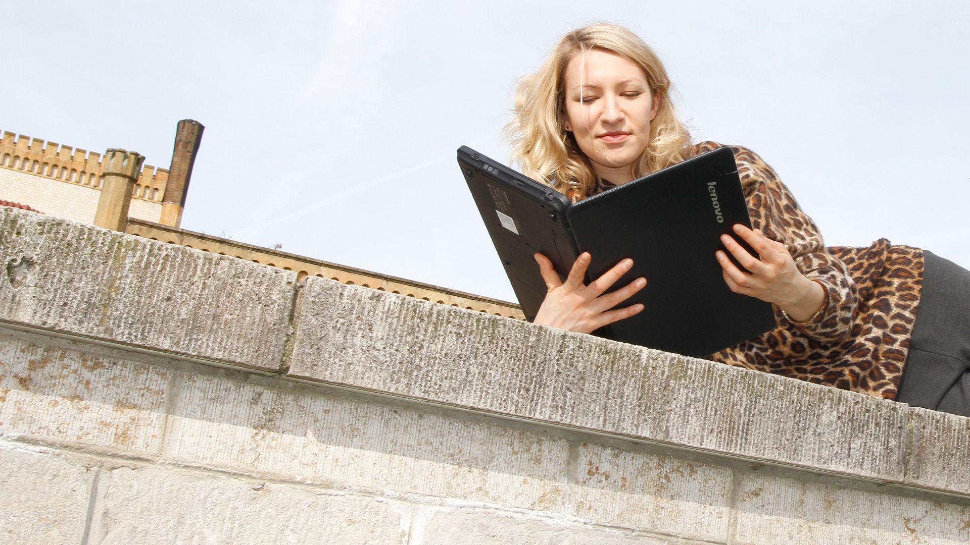 Mann sitzt auf Balkon und liest in einem Laptop Eine Frau liest in einem Laptop