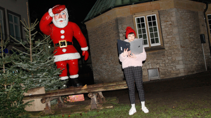 Eine Frau steht neben einem Weihnachtsbaum und einer Nikolaus-Figur und liest in ihrem Laptop