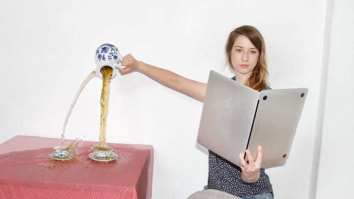 Eine Frau liest in einem laptop wie in einem Buch und vergiesst dabei Tee