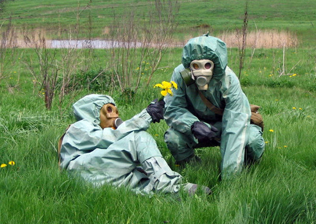 Zwei Menschen in Sicherheitskleidung und Gasmasken liegen auf einer Wiese