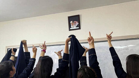 Viele junge Frauen halten einem Foto eines iranischen Politikers den Mittelfinger entgegen