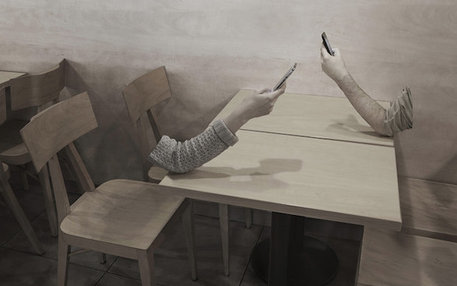 Zwei körperlose Arme, auf einen Tisch abgestützt, halten ein Smartphone in der Hand