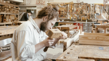 Ein Mann in einer Werksatt bearbeitet ein Stück Holz