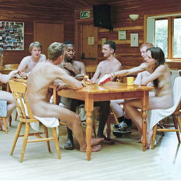 Junge Nudist_innen sitzen an einem Holztisch. Foto: Laura Pannack