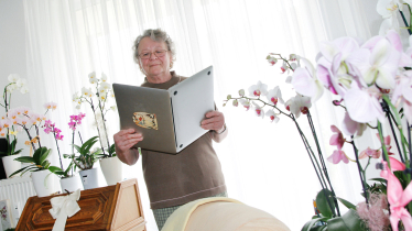 Von Orchideen umringte Frau hält Laptop wie ein Buch und liest darin