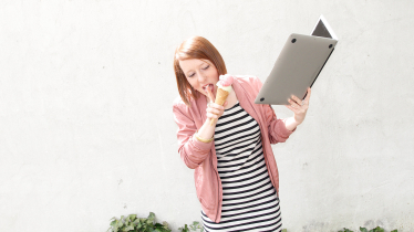Ein Mädchen ist Eis und hält dabei ein aufgeklapptes Laptop in den Händen Ein Mädchen ist Eis und hält dabei ein aufgeklapptes Laptop in den Händen