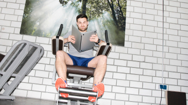 Mann auf Sportgerät liest in einem Laptop