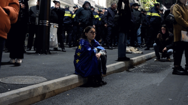 Eine junge Frau sitzt in eine Europa-Flagge gehüllt auf dem Gehweg