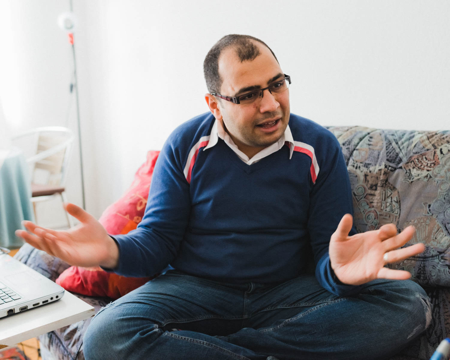 Der Syrer Aziz sitzt auf dem Sofa, erzählt und gestikuliert lebhaft (Foto: Christian Protte)